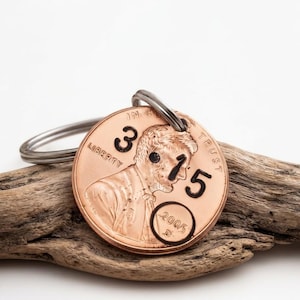 May include: A copper-colored metal keychain featuring a United States penny coin with the number 3 stamped in black ink above the portrait and the number 15 stamped to the right. The year 2005 is circled in black ink at the bottom right.