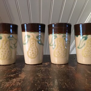 May include: Set of four brown and white ceramic mugs with a pear design. Each mug has a brown rim and a pear with green leaves painted on the front.