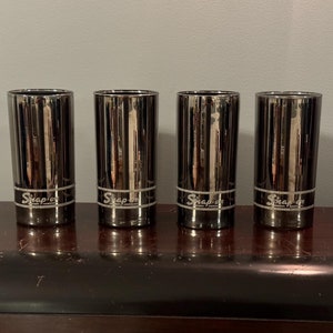 May include: Four black metal Snap-on brand drinking glasses with a silver logo.