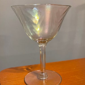 May include: A clear glass martini glass with an iridescent finish. The glass has a wide bowl and a long, thin stem.