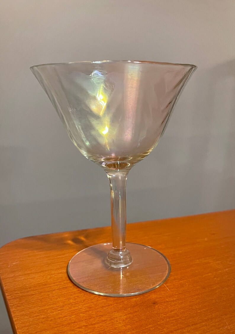 May include: A clear glass martini glass with an iridescent finish. The glass has a wide bowl and a long, thin stem.