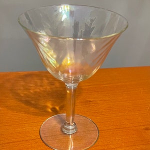 May include: A clear glass martini glass with a swirling pattern. The glass has an iridescent finish that shimmers in the light.