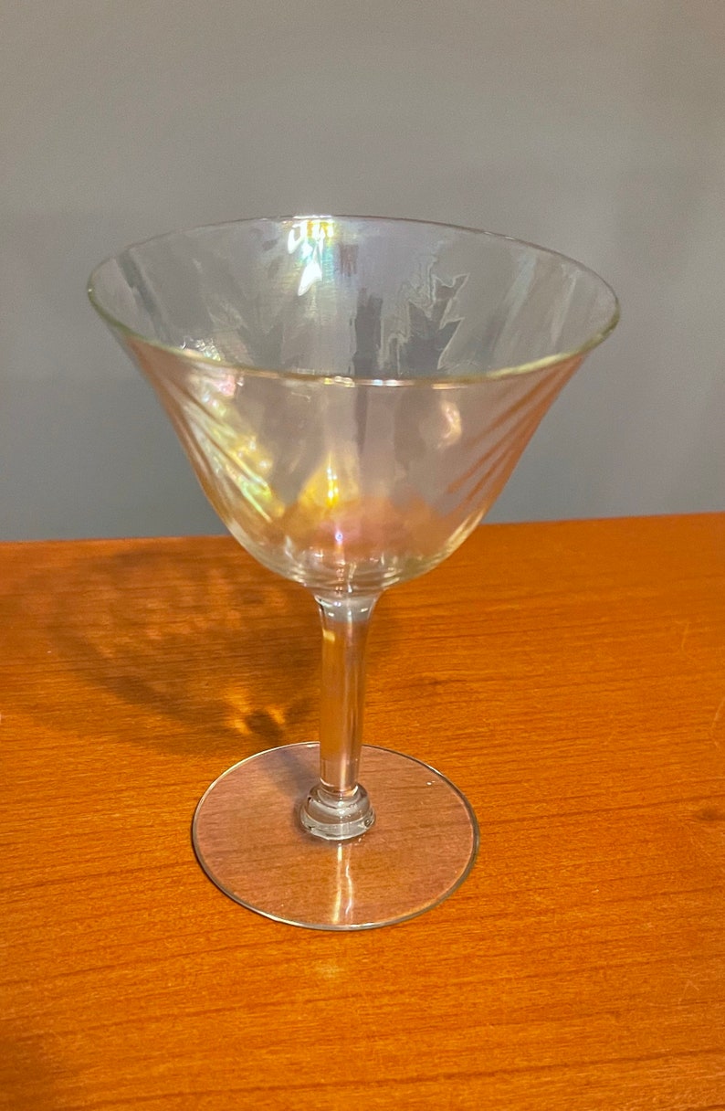 May include: A clear glass martini glass with a swirling pattern. The glass has an iridescent finish that shimmers in the light.