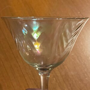 May include: A clear glass martini glass with a wide bowl and a long stem. The glass is empty and reflects light, creating a rainbow effect.