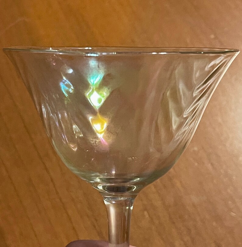 May include: A clear glass martini glass with a wide bowl and a long stem. The glass is empty and reflects light, creating a rainbow effect.