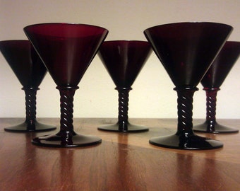 May include: Five black stemmed martini glasses with a twisted stem design. The glasses are arranged in a row on a wooden surface.