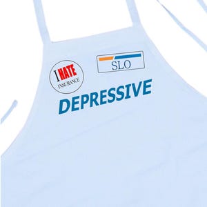 May include: Light blue apron with a red and white circle that says "I HATE INSURANCE" and a blue rectangle that says "DEPRESSIVE". There is also a yellow and blue rectangle that says "SLO".