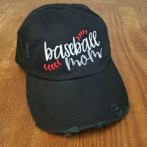 K&ouml;nnte beinhalten: Schwarze Baseballkappe mit abgenutzten Details. Die Kappe ist mit wei&szlig;er Stickerei versehen, die "baseball mom" lautet, mit roten N&auml;hten um das Wort "baseball".