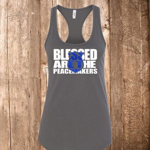 May include: A gray racerback tank top with the text "BLESSED ARE THE PEACEMAKERS" in white block letters. The word "PEACEMAKERS" is in a smaller font. The center of the text has a blue glitter design.