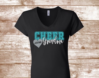 May include: Black v-neck t-shirt with a turquoise glitter design that says "Cheer Grandma" with a silver heart that says "Justine" on it.