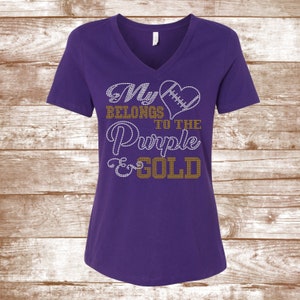 May include: Purple and gold V-neck t-shirt with rhinestones that spell out "My heart belongs to the Purple & Gold".