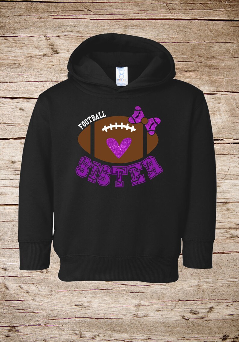 May include: Black hooded sweatshirt with a purple glitter football design and the text "Football Sister".