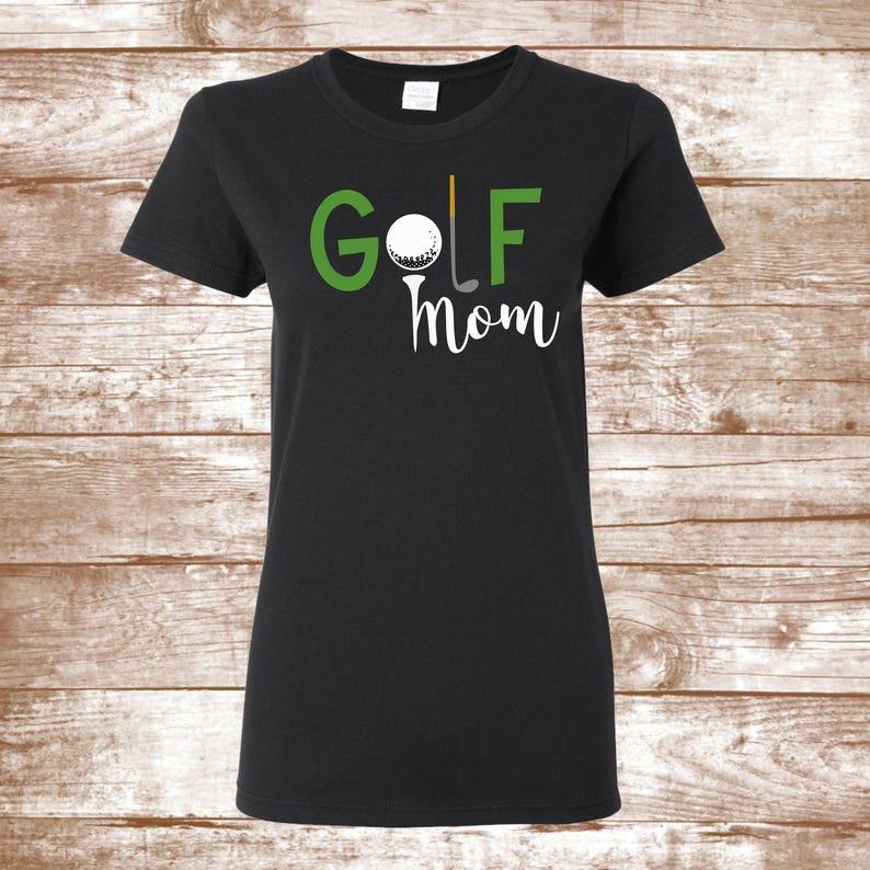 Puede incluir: Camiseta negra con el texto "GOLF MOM" en verde y blanco. Un palo de golf y una bola de golf est&aacute;n incluidos en el texto.