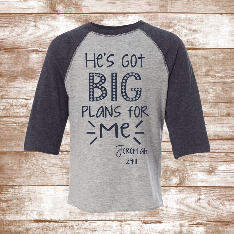 May include: A gray and navy blue baseball tee shirt with the text "He's got BIG PLANS for ME" and "Jeremiah 29:11" printed on the front.