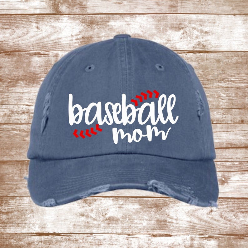 K&ouml;nnte beinhalten: Eine blaue Baseballkappe aus Denim mit Used-Look. Die Kappe hat eine wei&szlig;e Stickerei mit der Aufschrift "baseball mom" und rote N&auml;hte um das Wort "baseball".