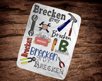 May include: White blanket with the name "Brecken" in various fonts and colors, along with illustrations of tools like a wrench, hammer, and toolbox. The word "grey" is also included.
