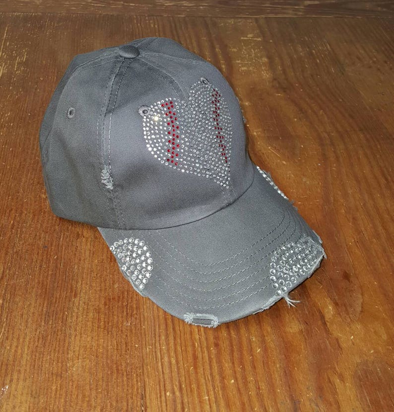 Op de afbeelding: Een grijze baseballpet met een distressed look. De voorkant van de pet heeft een hart van strass met een rood baseballsteekontwerp.