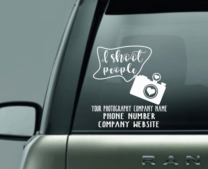 May include: White vinyl decal for a car window. The decal features the text "I shoot people" in a stylized font, along with a camera graphic with a heart in the lens. Additional text includes space for a photography company name, phone number, and website.