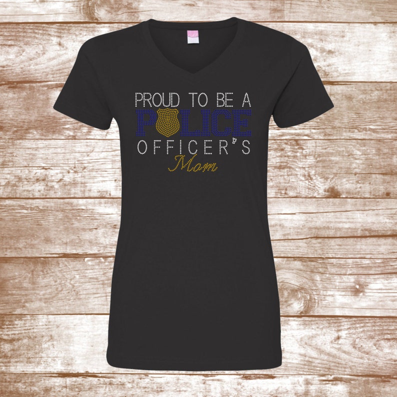 Puede incluir: Camiseta negra de cuello en V con el texto "Proud to be a Police Officer's Mom" en pedrer&iacute;a azul y dorada.