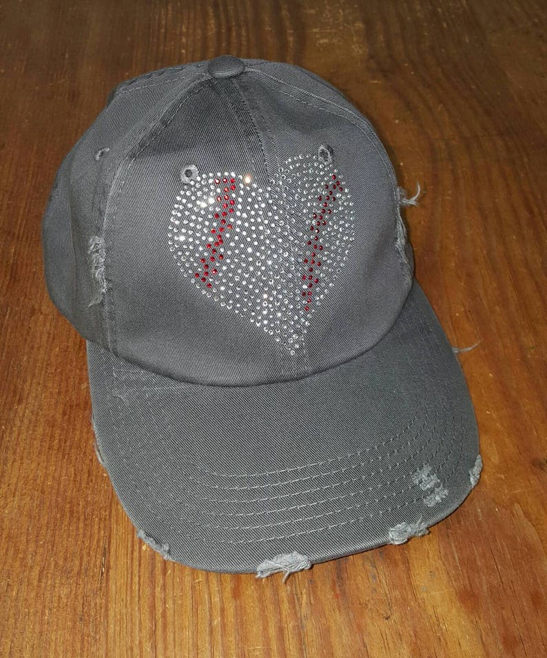 Op de afbeelding: Een grijze, verweerde baseballpet met een strass-baseballhartontwerp. Het hart is rood omrand.
