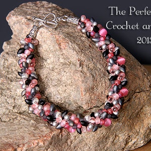 May include: A multi-strand beaded bracelet with pink, black and grey beads. The bracelet has a silver clasp and is displayed on a rock.