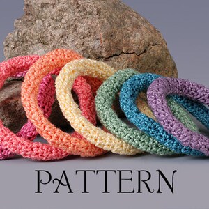 Puede incluir: Un conjunto de siete pulseras de ganchillo en un arcoíris de colores, incluyendo rosa, naranja, amarillo, verde, azul y morado. Las pulseras están apiladas una encima de la otra, con la pulsera más grande en la parte inferior y la más pequeña en la parte superior.