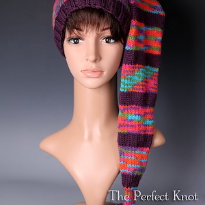 May include: A purple and multi-colored striped knit hat with a long tail and a pom-pom. The hat is on a mannequin's head. The text "The Perfect Knot Crochet and More 2013" is at the bottom of the image.