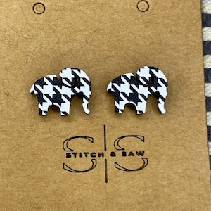 May include: A pair of black and white houndstooth elephant stud earrings. The earrings are made of wood and have a simple, elegant design.
