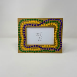 May include: A rectangular wooden picture frame with a decorative border of green, yellow, and purple beads. The frame has a white interior with a drawing of a goose and the text "Tomato + Goose".