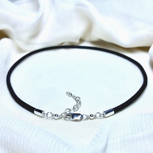 May include: A black cord necklace featuring a silver-toned lobster claw clasp and an adjustable chain extender. The cord is secured at both ends with silver-toned metal caps, and the clasp assembly includes small silver-toned beads for detail.