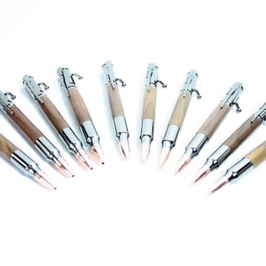 May include: Ten wooden pens with silver accents and a bullet casing design. The pens are arranged in a semi-circle on a white background.