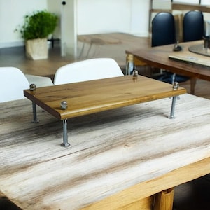 May include: A wooden laptop stand with metal legs. The stand is made of natural wood and has a rustic look. It is sitting on a wooden table.