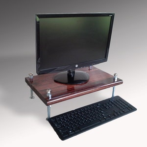 May include: A dark wood monitor stand with a black computer keyboard. The stand has a rectangular top and is supported by four metal legs. A black computer monitor is on top of the stand.