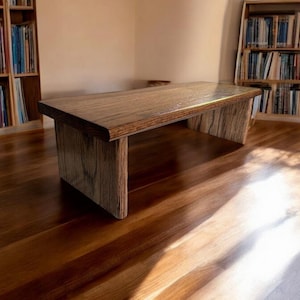May include: A wooden coffee table with a natural wood finish. The table has a rectangular top and two rectangular legs. The table is sitting on a wooden floor.