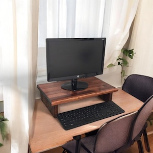 May include: A wooden monitor stand with a black computer monitor and keyboard on a wooden desk. The monitor stand is raised to an ergonomic height.