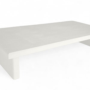 May include: A white, rectangular coffee table with a simple, modern design. The table has a flat top and two open, rectangular supports on either side.