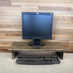 May include: A dark wood monitor stand with a black computer monitor and keyboard on a light gray surface.