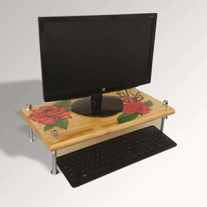 May include: A wooden computer monitor stand with a floral design featuring red roses. The stand has a lower shelf for a keyboard.