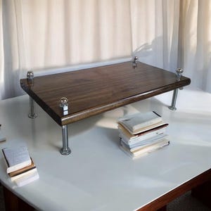 May include: A dark brown wooden desk riser with metal legs. The riser is sitting on a white surface with a stack of books underneath.