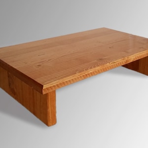 May include: A wooden riser with a natural finish. The riser is rectangular and has a flat top surface. It is made of solid wood and has a simple, modern design.
