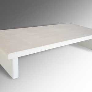 May include: White coffee table with a rectangular top and two white supports. The table is made of wood and has a simple, modern design.