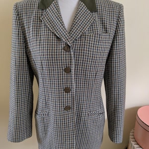May include: A brown, blue, and white houndstooth patterned blazer with a green velvet collar. The blazer has four buttons down the front.