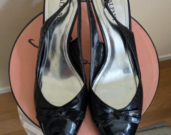 May include: A pair of black patent leather slingback heels with a peep toe design. The shoes have a bow detail on the vamp and a silver insole. The heels are approximately 3 inches high.