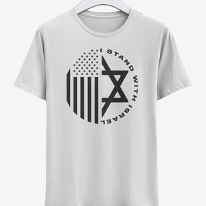 May include: White t-shirt with a circular graphic featuring the American flag and a Star of David. The text "I STAND WITH ISRAEL" is printed around the star in black.