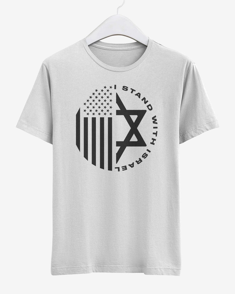 May include: White t-shirt with a circular graphic featuring the American flag and a Star of David. The text "I STAND WITH ISRAEL" is printed around the star in black.