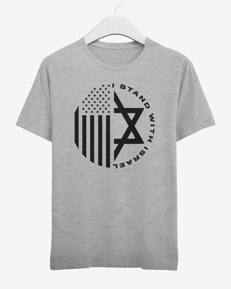 May include: A grey t-shirt with a circular graphic incorporating the American flag and a Star of David. The black text reads "I STAND WITH ISRAEL". The t-shirt is displayed on a white hanger.