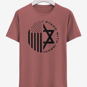 May include: A dusty rose t-shirt with a black graphic. The graphic features a circular design with the American flag on the left and a Star of David on the right, with the text "I STAND WITH ISRAEL" around the circle.