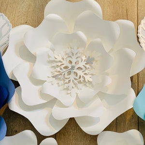 May include: A large white paper flower with a snowflake in the center. The snowflake is white with a silver glitter center.