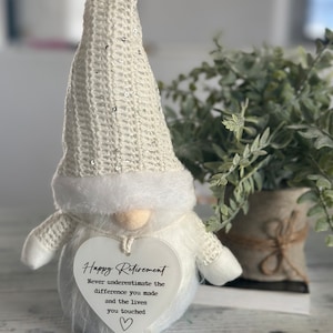 May include: White gnome figurine with a heart-shaped sign that reads "Happy Retirement Never underestimate the difference you made and the lives you touched".