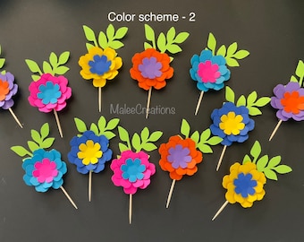 May include: Twelve paper flower cupcake toppers with light green leaves, each attached to a wooden toothpick. The flowers feature layered petals in various color combinations including yellow, orange, blue, purple, and pink. Text reads Color scheme - 2 and MaleeCreations.